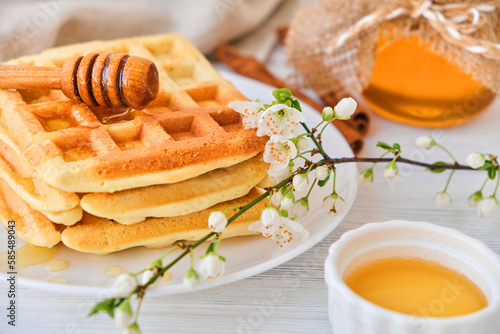 Honey pouring on a fresh Belgian waffles. Organic healthy Spring breakfast rich in minerals and vitamins. Eco food for breakfast. Trendy sweet confections with cherry blossoms