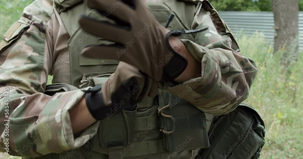 Unrecognizable female soldier in camouflage uniforms , getting ready for military exercises or battle. Detailed shot of military woman putting on tactical gloves. Ukrainian army, war, slow motion Unrecognizable female soldier in camouflage uniforms , getting ready for military exercises or battle. Detailed shot of military woman putting on tactical gloves. Ukrainian army, war, slow motion