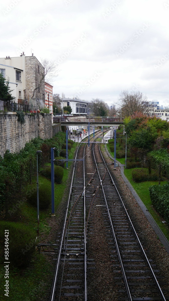 Lignes de rail de métro ou de RER dans une zone urbaine, vide, dans la nature, sans passage de train et sous un temps humide, après passage de pluie, industriel ferroviaire, sous un ciel nuageux