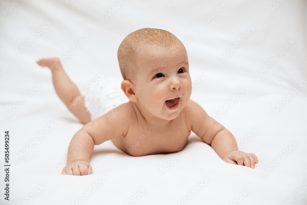 A newborn baby in a diaper is lying on stomach and laughing on a white background. A newborn baby in a diaper is lying on stomach and laughing on a white background.