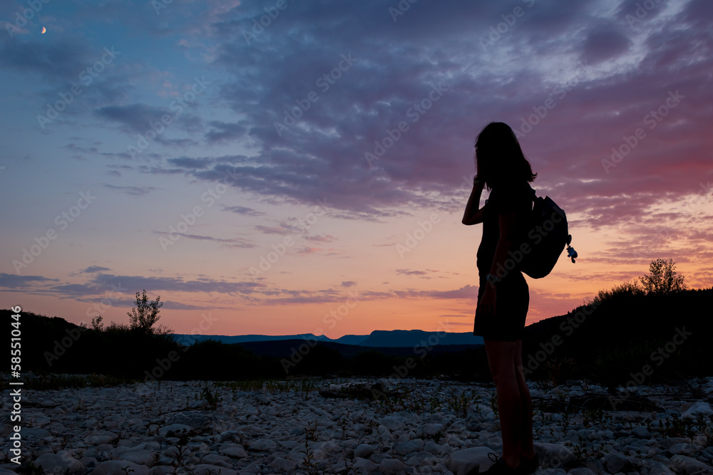 Fototapeta premium A silhouette of a female traveler standing in the mountains during sunset