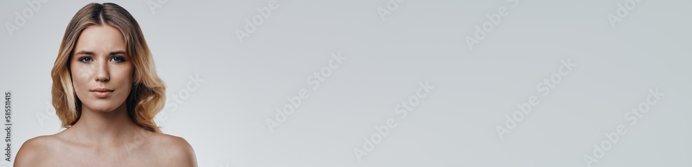 Attractive young blonde hair woman looking at camera while standing against grey background Attractive young blonde hair woman looking at camera while standing against grey background