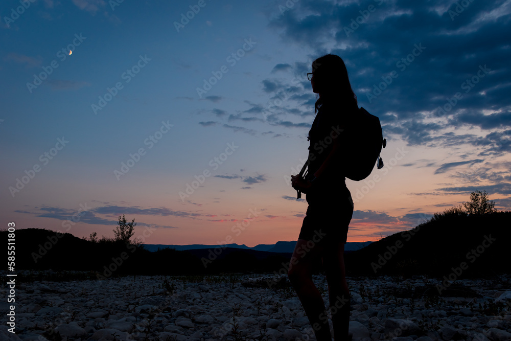 A silhouette of a female traveler standing in the mountains during sunset