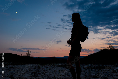 A silhouette of a female traveler standing in the mountains during sunset