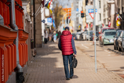 Man with red vest and a bag walking on the street side walk at sunny day © Kaspars