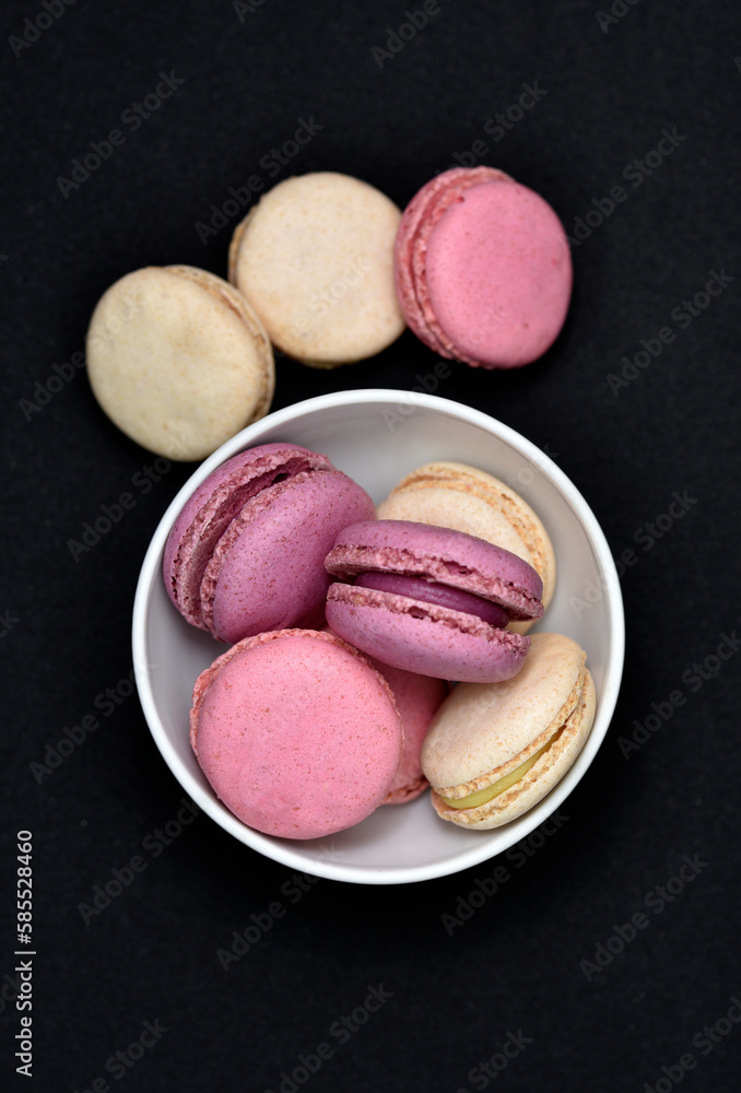 Macaroons in a white plate on a black background. Macaroons in a ceramic bowl. Colorful sweet cookies. Macaroons in a white plate on a black background. Macaroons in a ceramic bowl. Colorful sweet cookies.