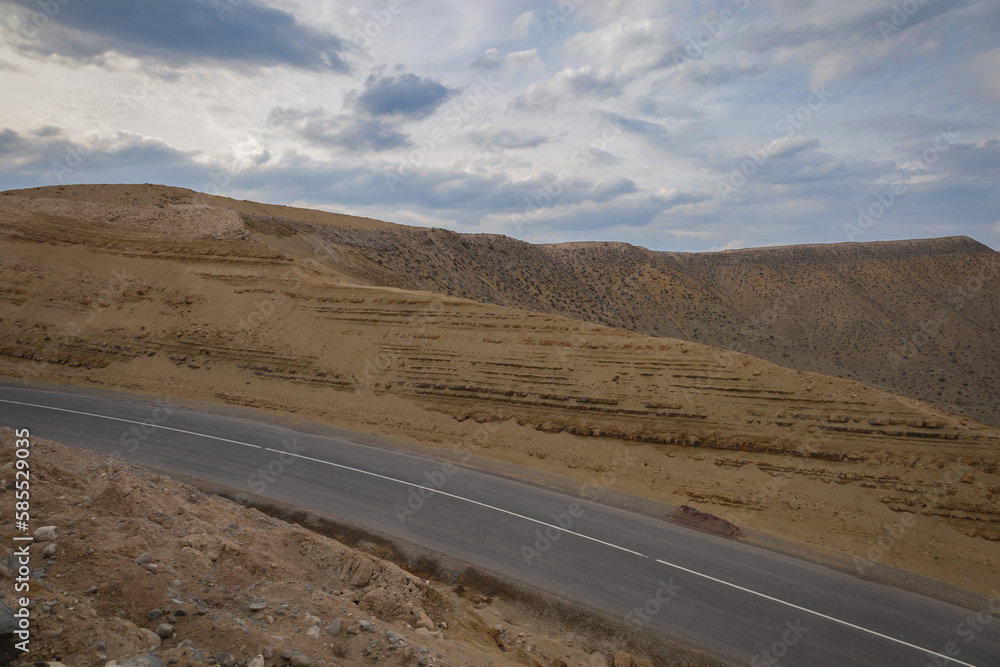 Highway passing through arid mountains on a beautiful cloudy day. Strips on a hillside. Soil erosion, roadside slope.
