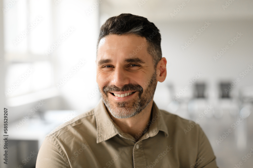 Portrait of well dressed middle aged businessman smiling confidently while standing in light modern office interior Portrait of well dressed middle aged businessman smiling confidently while standing in light modern office interior