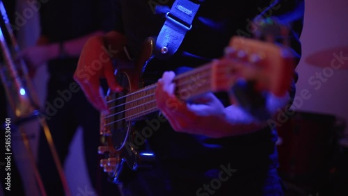 Guitarist plays bass guitar on stage during concert, close-up. Musician actively moves to beat of music. Trumpeter of musical band is dancing. Colored multi-colored light rhythmically changes.