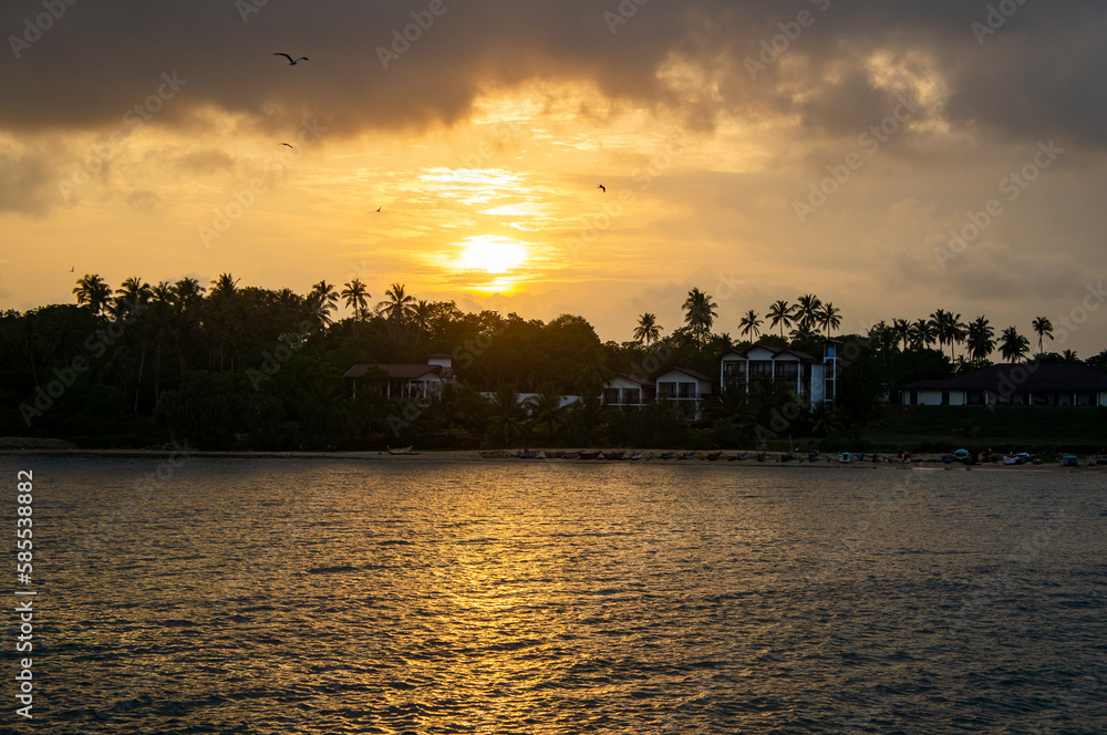 Very beautiful tropical coast at golden sunset. Black silhouette of the coast with palm trees and hotels. Photography for tourism, design and advertising