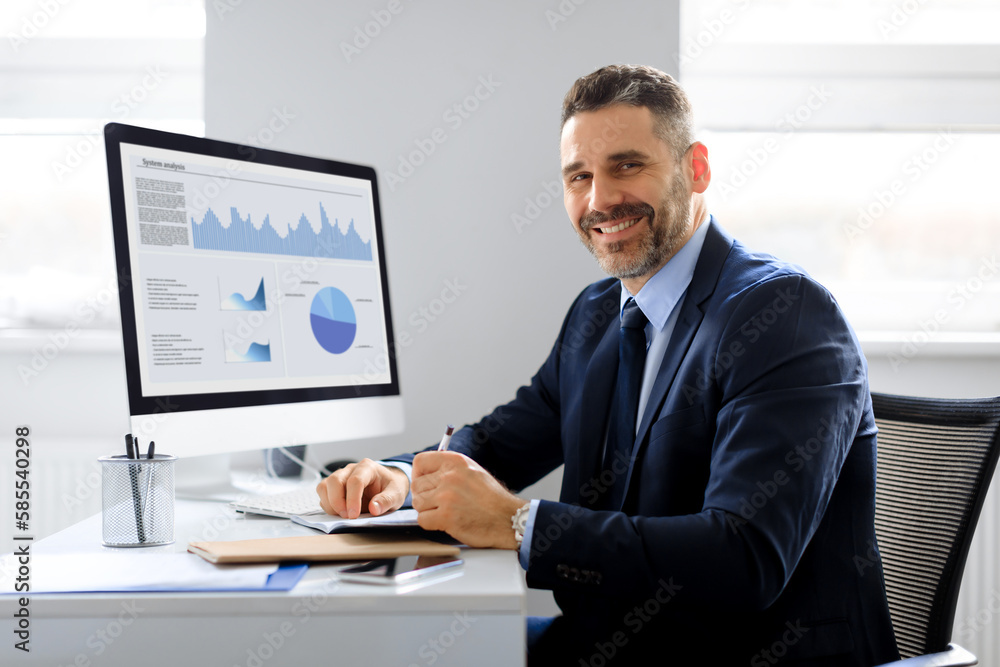 Portrait of happy businessman working on computer in office and smiling at camera, monitor with graphics and charts Portrait of happy businessman working on computer in office and smiling at camera, monitor with graphics and charts