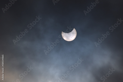 Partial eclipse of the sun on a cloudy sky with visible sunspots on its surface.