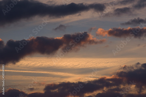 The sky with dark blue clouds illuminated by warm orange light of the setting sun.