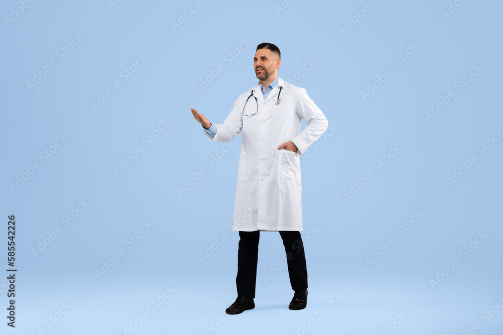 Middle aged doctor man showing copy space with hand, wearing uniform, walking on blue studio background, full length