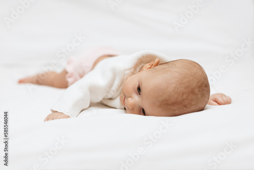 A newborn girl in a white knitted blouse is lying on a white blanket.