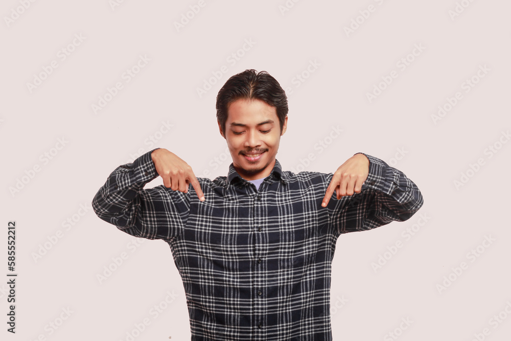 Fototapeta premium Happy slim asian man wearing casual clothes standing pointing index finger down on dummy copy space isolated on background.