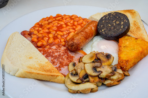 White board with full English breakfast with bacon, fried egg, beans, tomato, roasted sausage, black pudding, scons, hash browns and fried mushrooms photo