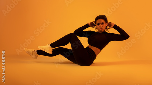 Fitness workout. Black sportswoman in fitwear doing elbow to knee abs crunch exercising on neon orange sudio background photo
