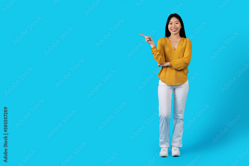 Cheery young asiam lady pointing at copy space on blue Cheery young asiam lady pointing at copy space on blue