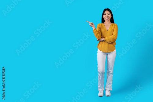 Cheery young asiam lady pointing at copy space on blue