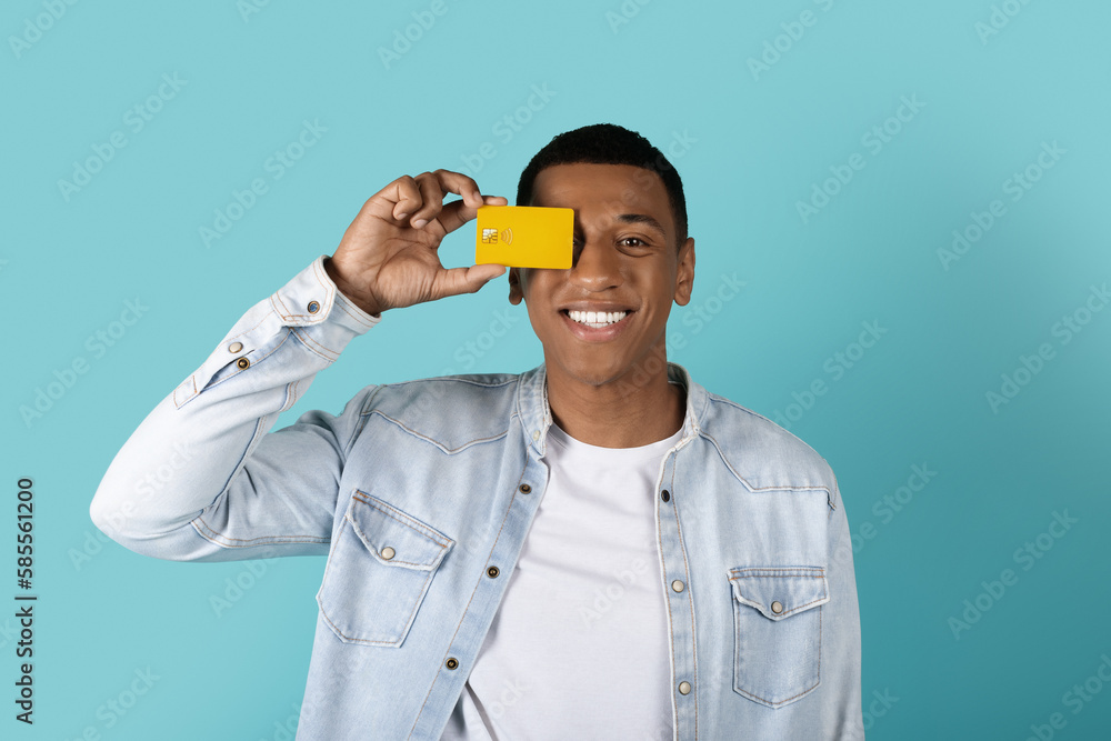 Happy funny millennial black male in casual puts credit card to eye, recommends saving Happy funny millennial black male in casual puts credit card to eye, recommends saving