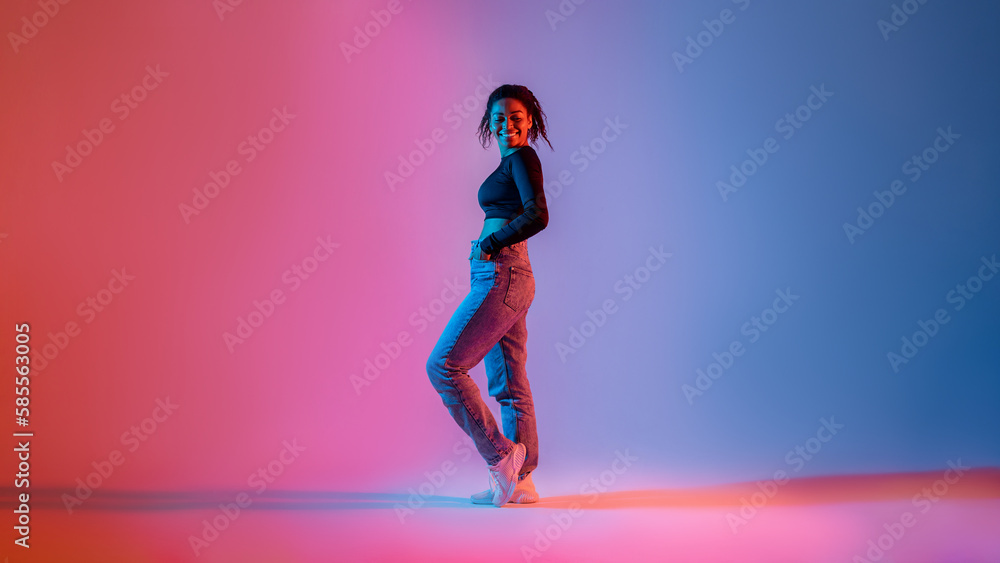 Full length of stylish african american woman posing in neon light in studio and smiling at camera