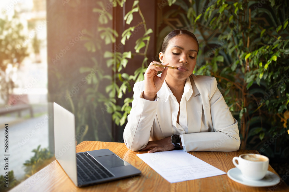 Thoughtful serious concentrated young black lady in suit writes on paper, thinks with laptop, enjoy coffee Thoughtful serious concentrated young black lady in suit writes on paper, thinks with laptop, enjoy coffee