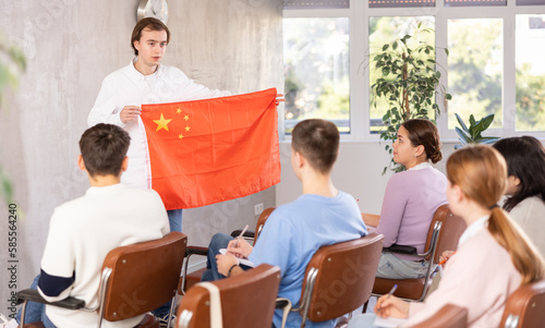 Young man tells his classmates the history of the state of China  holding the national flag of Chinese in his hands