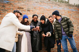 Mixed group of friends smiling and enjoying stay together. Happy people laughing using smartphone in outdoors during cold season.