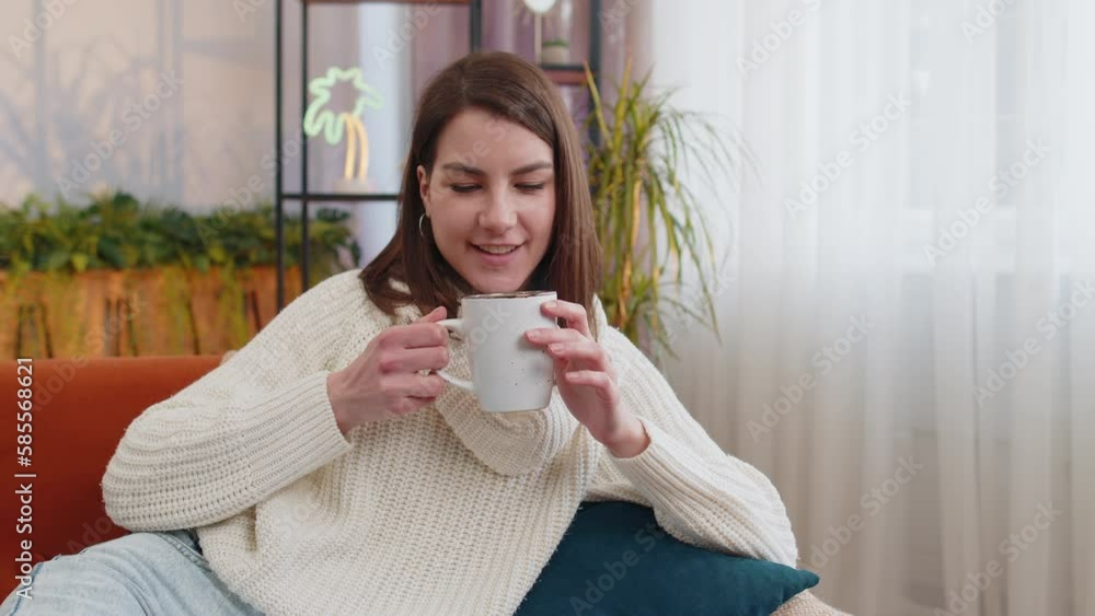 Portrait of attractive smiling young woman drinking a cup of warm coffee or herbal tea at home living room apartment in the morning. Pretty girl lying on couch enjoying comfortable relaxing alone Portrait of attractive smiling young woman drinking a cup of warm coffee or herbal tea at home living room apartment in the morning. Pretty girl lying on couch enjoying comfortable relaxing alone