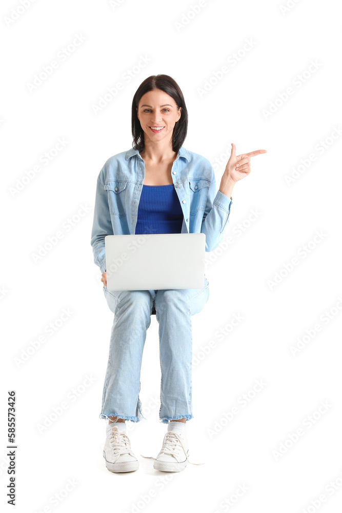 Pretty young woman with laptop pointing at something while sitting on chair against white background Pretty young woman with laptop pointing at something while sitting on chair against white background
