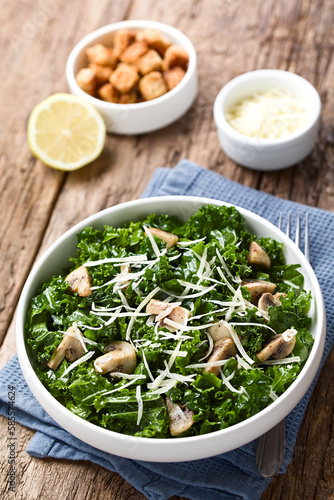 Fresh raw curly kale and sauteed mushroom salad with grated parmesan served in bowl, photographed on wood (Selective Focus, Focus one third into the image)