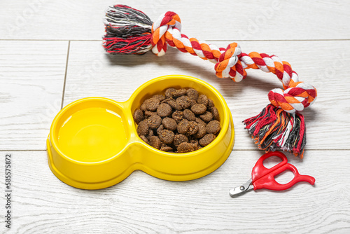 Bowl with dry pet food, nail clipper and toy on light wooden background