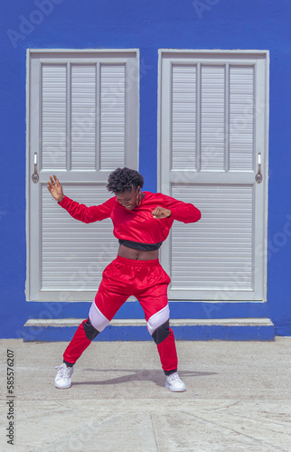 Jover mujer afro realiza baile estilo urban en parque local con pared azul y puertas de fondo photo