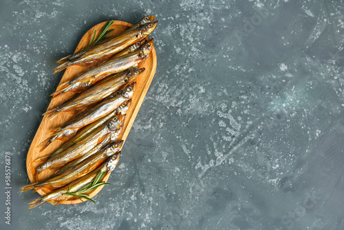 Board with delicious smoked capelin and rosemary on grey grunge background photo