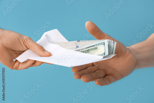 Doctor taking bribe from man on blue background, closeup