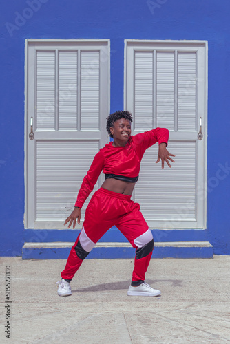 Jover mujer afro realiza baile estilo urban en parque local con pared azul y puertas de fondo photo