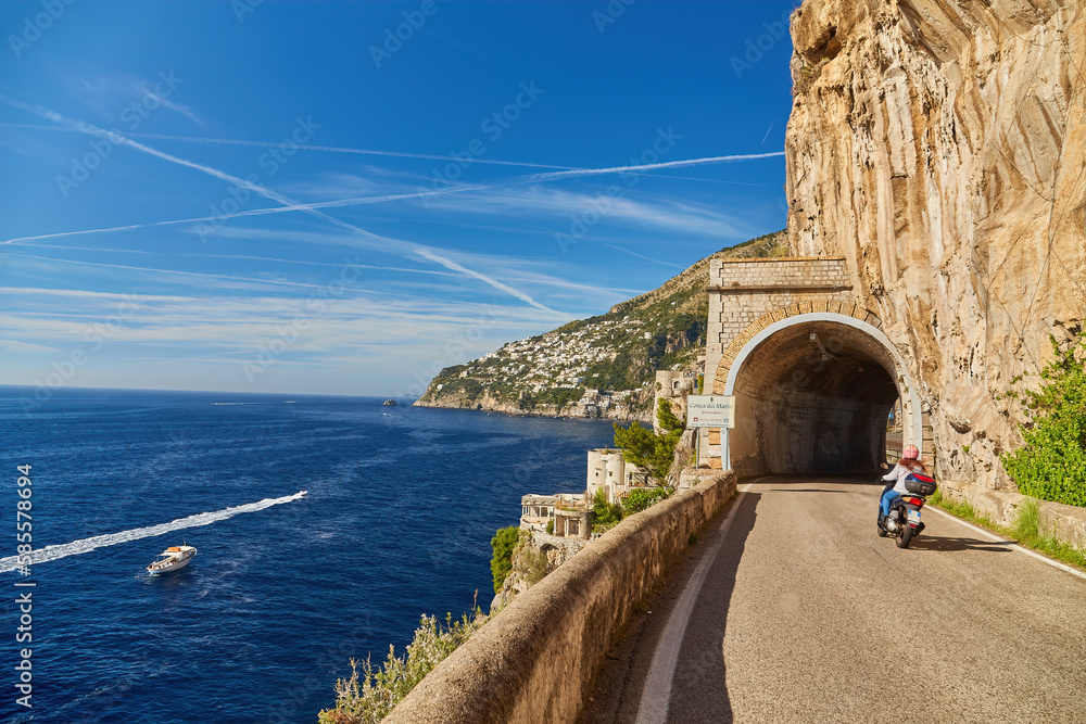 Scooter drives along the road along the Amalfi coast, approaching the tunnel Conca dei Marini