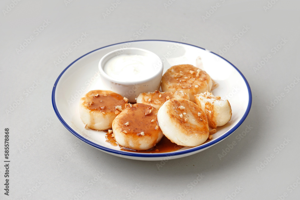 Plate of tasty cottage cheese pancakes with sour cream on light background