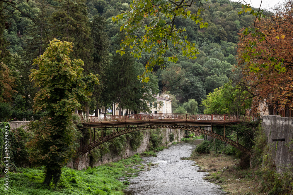Panorama of the river Cerna in Baile Herculane, with te podul de fonta, or cast iron bridge, a rusty vintage bridge, in the middle of the mountains in the romanian countryside.