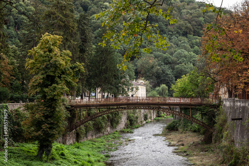 Panorama of the river Cerna in Baile Herculane, with te podul de fonta, or cast iron bridge, a rusty vintage bridge, in the middle of the mountains in the romanian countryside.