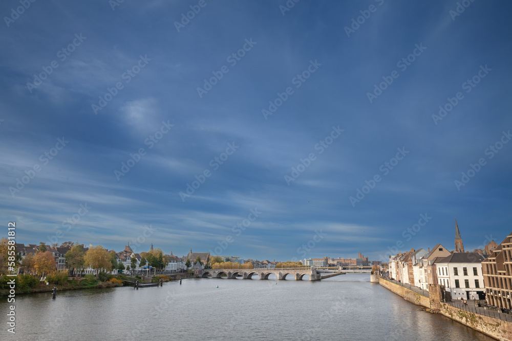 Fototapeta premium Panorama of Maastricht Waterfront on the Meuse Maas river with a focus on sint servaasbrug or saint servatius bridge, in autumn, during a sunny afternoon. Maastricht is a dutch city in the netherlands