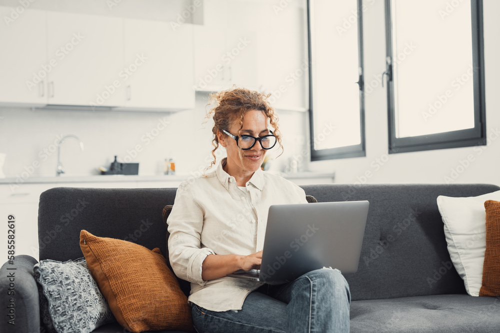 Smiling young woman using laptop, sitting on couch at home, beautiful girl shopping or chatting online in social network, having fun, watching movie, freelancer working on computer project. Smiling young woman using laptop, sitting on couch at home, beautiful girl shopping or chatting online in social network, having fun, watching movie, freelancer working on computer project.