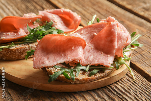 Board of tasty bruschettas with ham on wooden background, closeup