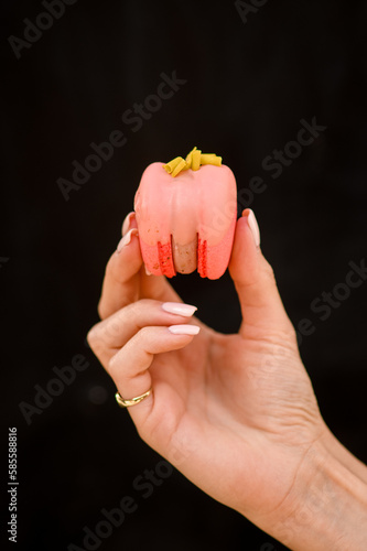 close-up of female hand neatly holds delicious sweet bright pink macaron on black background.