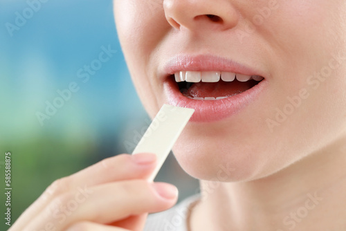 Woman putting chewing gum piece into mouth on blurred background, closeup