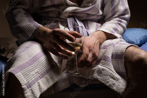 Man and alcoholism. An unrecognizable man in a bathrobe holds a glass of wine. Drink alcohol to fall asleep before bed.