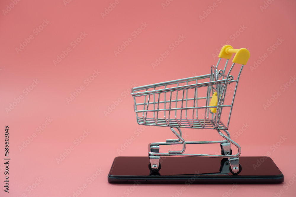 Empty shopping trolley and mobile phone on a pastel pink background. Shop basket for products. Online shopping on smartphone for a global concept. Empty shopping trolley and mobile phone on a pastel pink background. Shop basket for products. Online shopping on smartphone for a global concept.