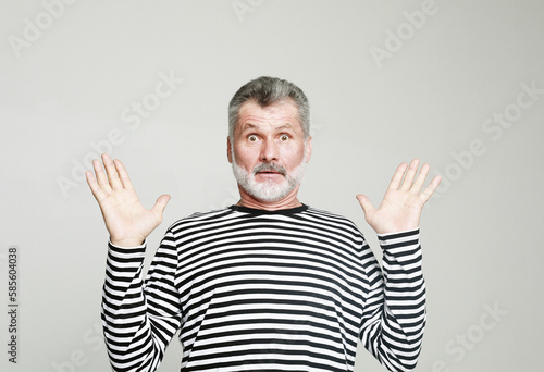 Surprised joyful elderly man with a gray beard raises his hands in amazement.