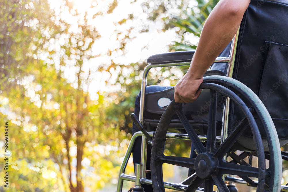 Man sitting in wheelchair with hand holding on wheel controller.Colorful tree on blur background.Wheelchair for elderly or people with disability.Close up photo.Yellow background with beautiful light Man sitting in wheelchair with hand holding on wheel controller.Colorful tree on blur background.Wheelchair for elderly or people with disability.Close up photo.Yellow background with beautiful light